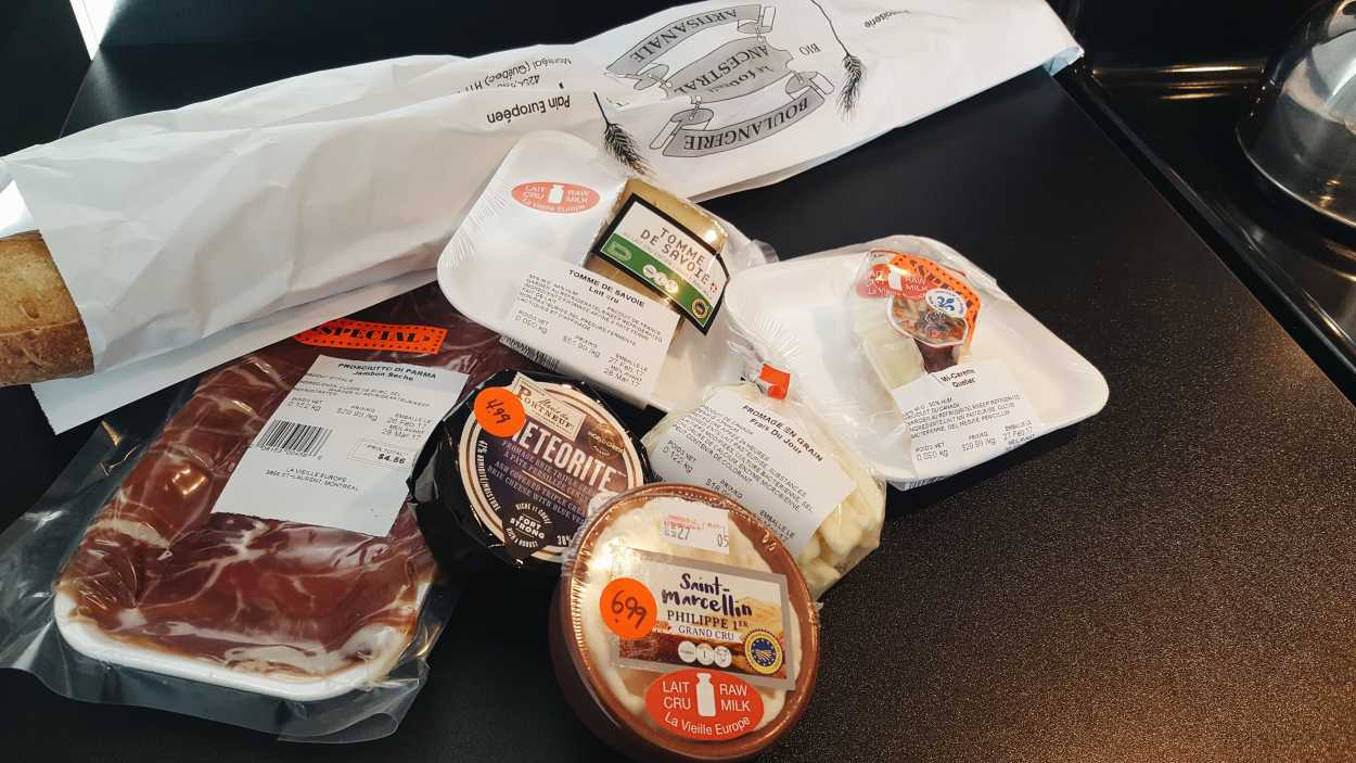 A counter with raw milk cheeses, meat, and a baguette