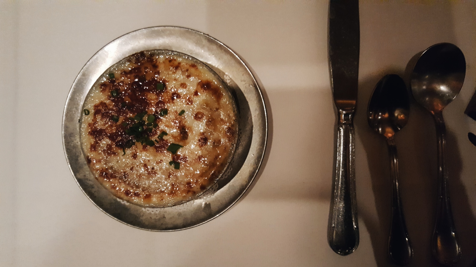 A bowl of French Onion Soup with silverware from Bern's. It is expertly prepared