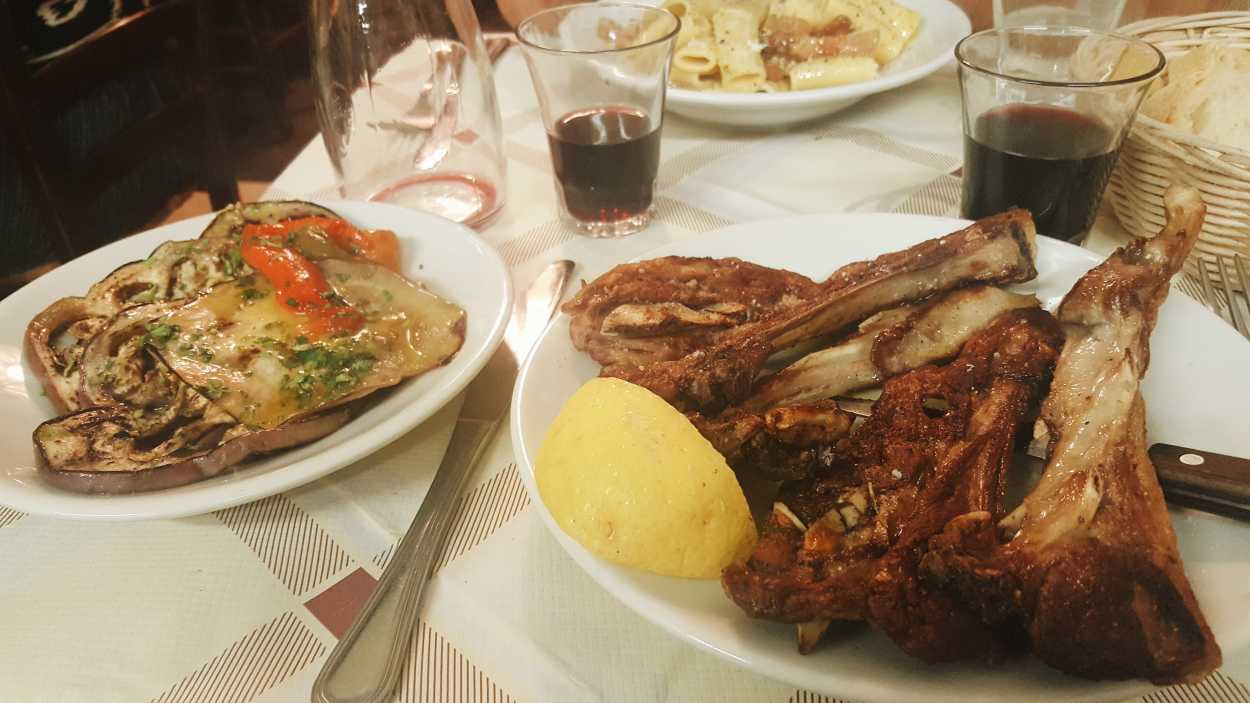 large pieces of lamb and grilled vegetables on a table with wine glasses