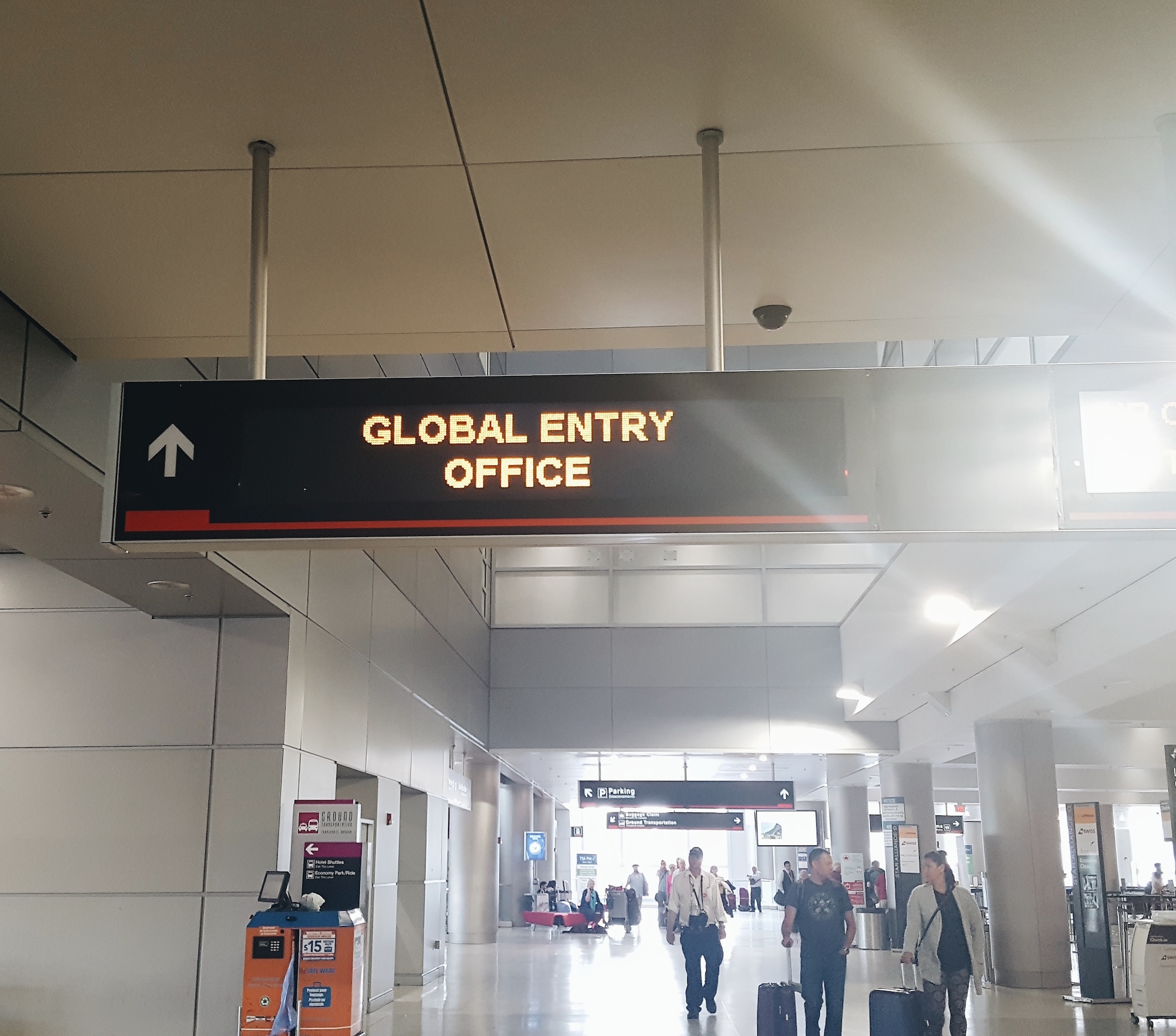 People walk in an airport under a sign that points to the Global Entry office