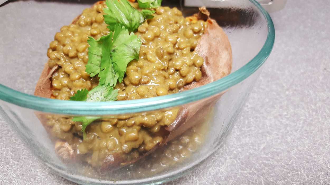 A sweet potato with Indian Spiced Black Dhal in a glass bowl