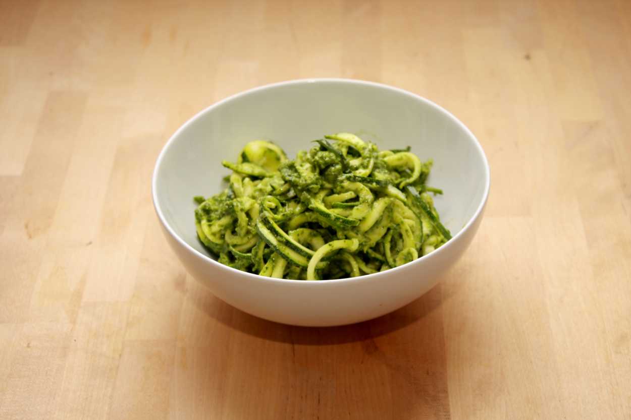 A white bowl containing Spiralized Zucchini Noodles with Mint Parsley Pepita Pesto