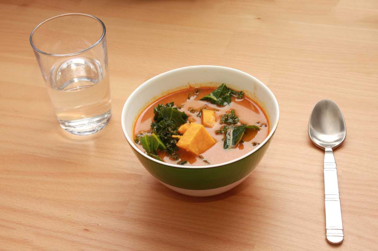A green bowl with Harissa Spiced Sweet Potato Soup and Kale