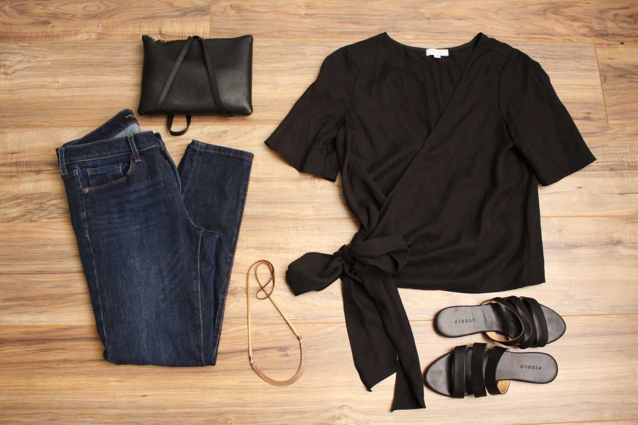 A wrap top, jeans, purse, and sandals are arranged on a wood floor in a flatlay