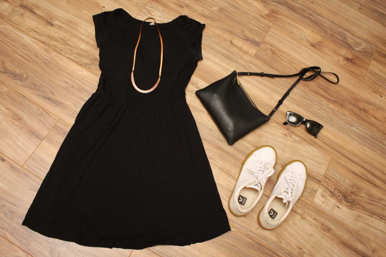 A dress, sneakers, and bag are arranged on a wood floor in a flatlay