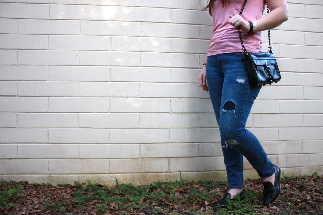 Alyssa stands in front of a white brick wall with a black purse