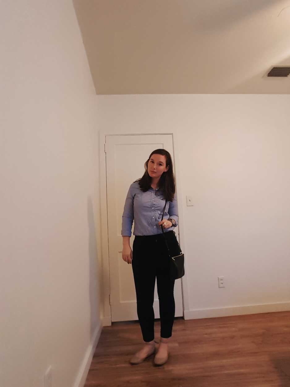 Alyssa wears a blue oxford shirt with black pants and beige flats in the evening