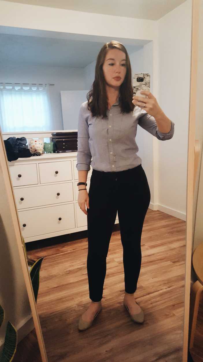Alyssa wears a blue oxford shirt with black pants and beige flats in the morning