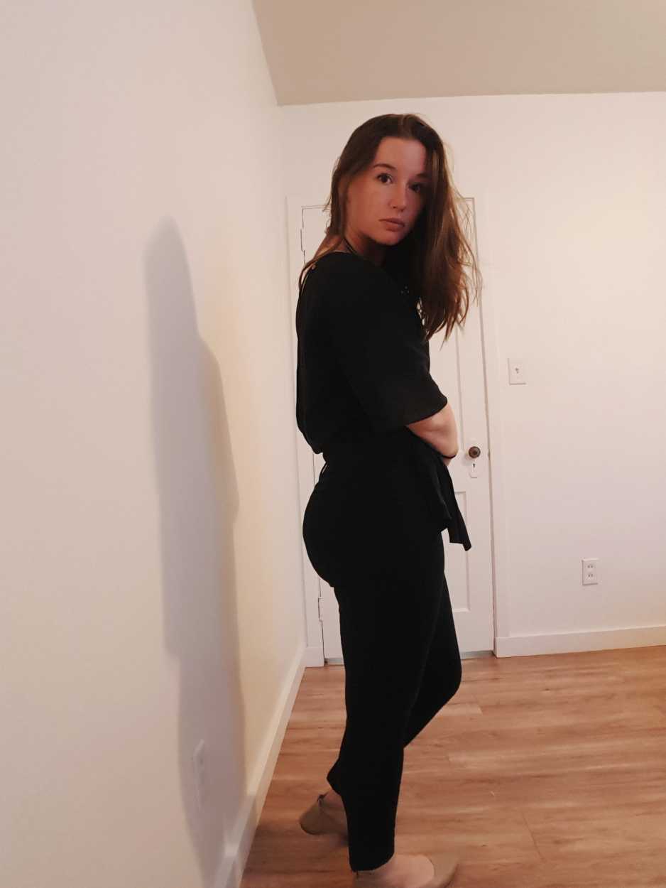 Alyssa wears black pants, a black wrap top, and beige flats in the evening