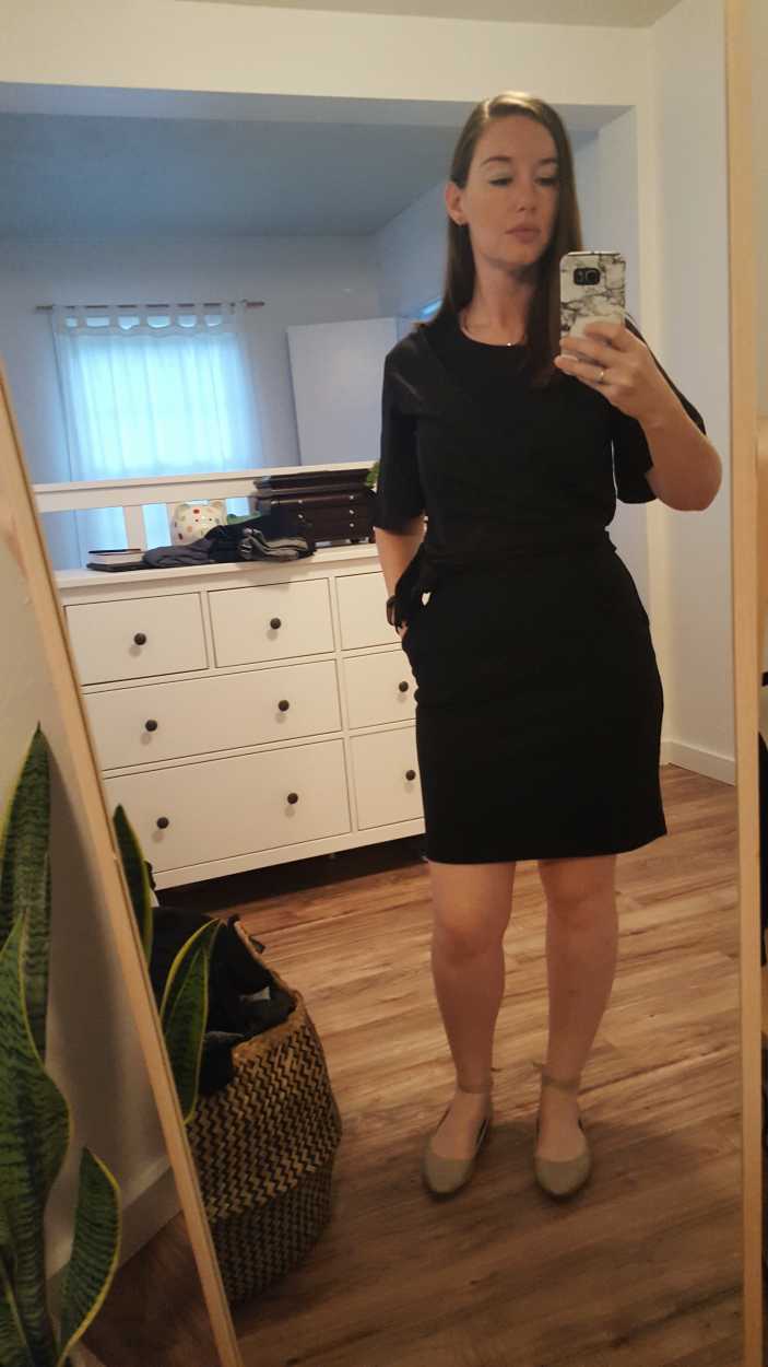 Alyssa wears a black wrap top over a black dress with tan shoes in the morning