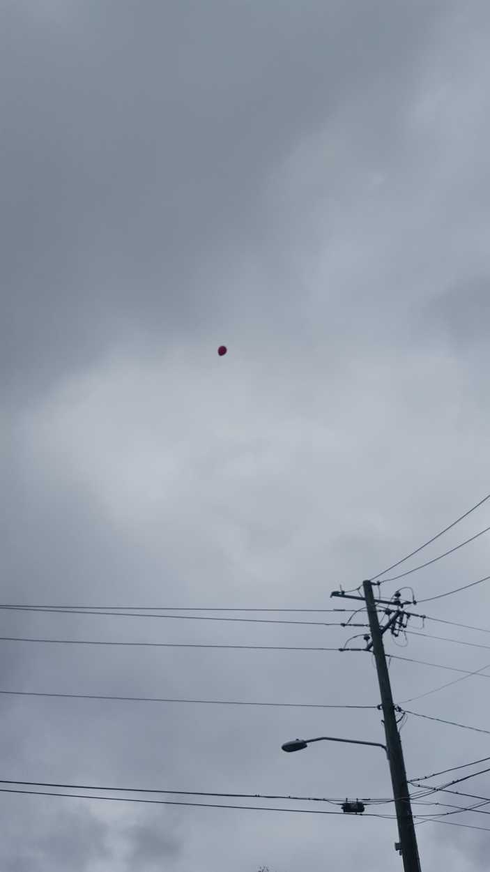 A red balloon lost and floating toward the clouds