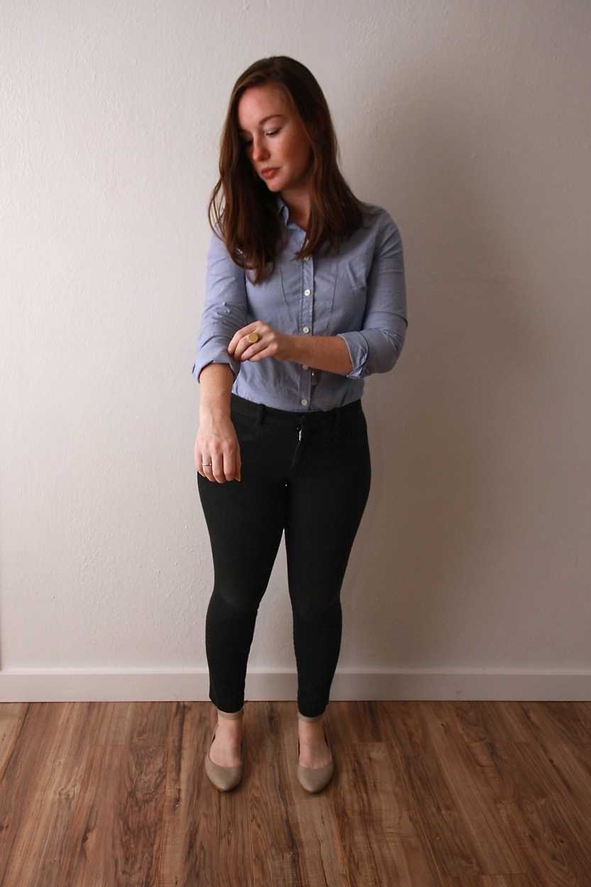 Alyssa wears a blue oxford shirt with black pants and beige flats and adjusts the sleeve on her top