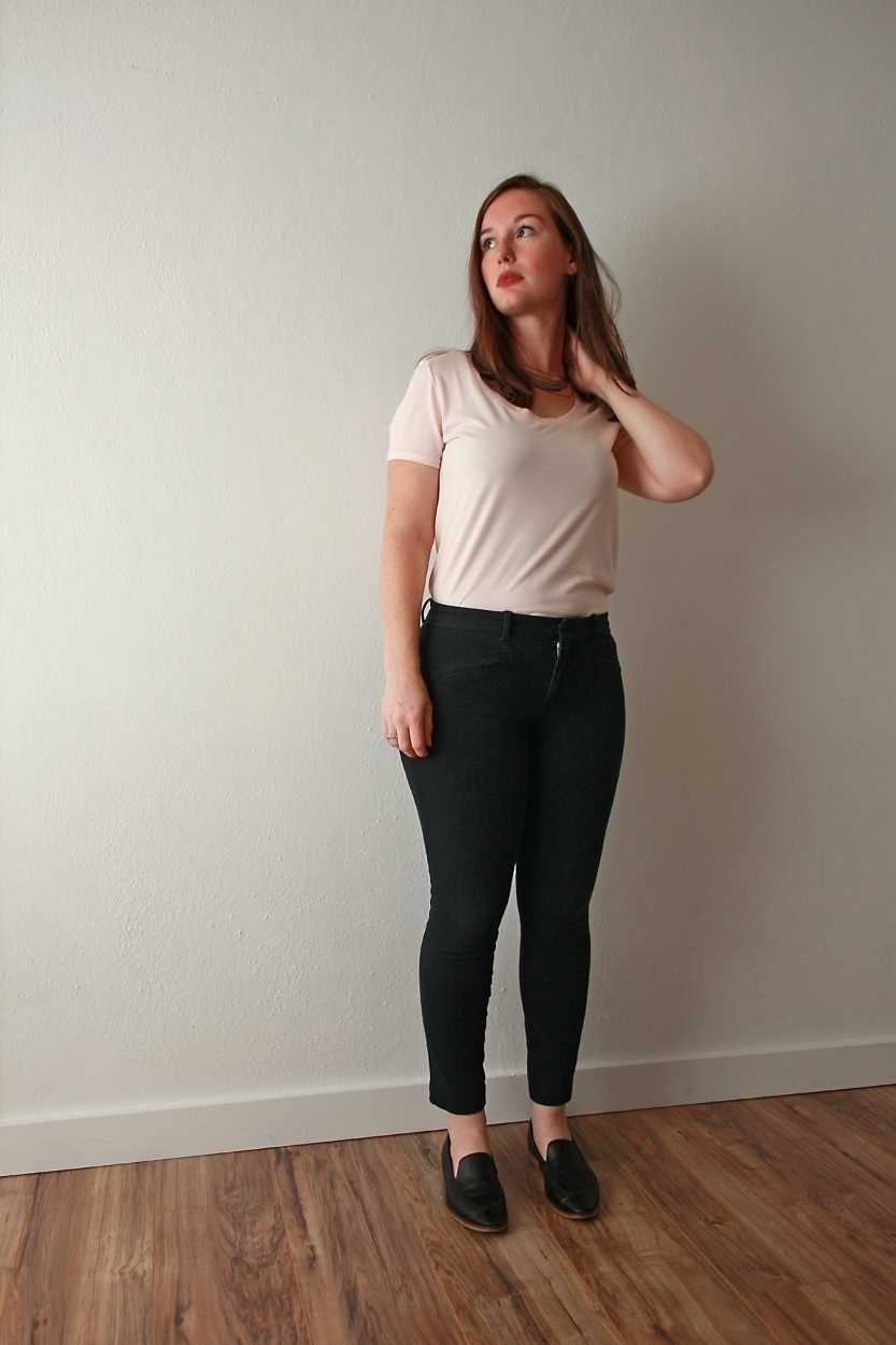 Alyssa wears a pink tee, black pants, black loafers and looks off camera