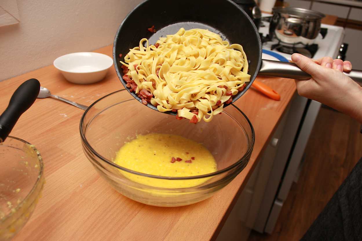 Alyssa pours the pasta into the carbonara sauce