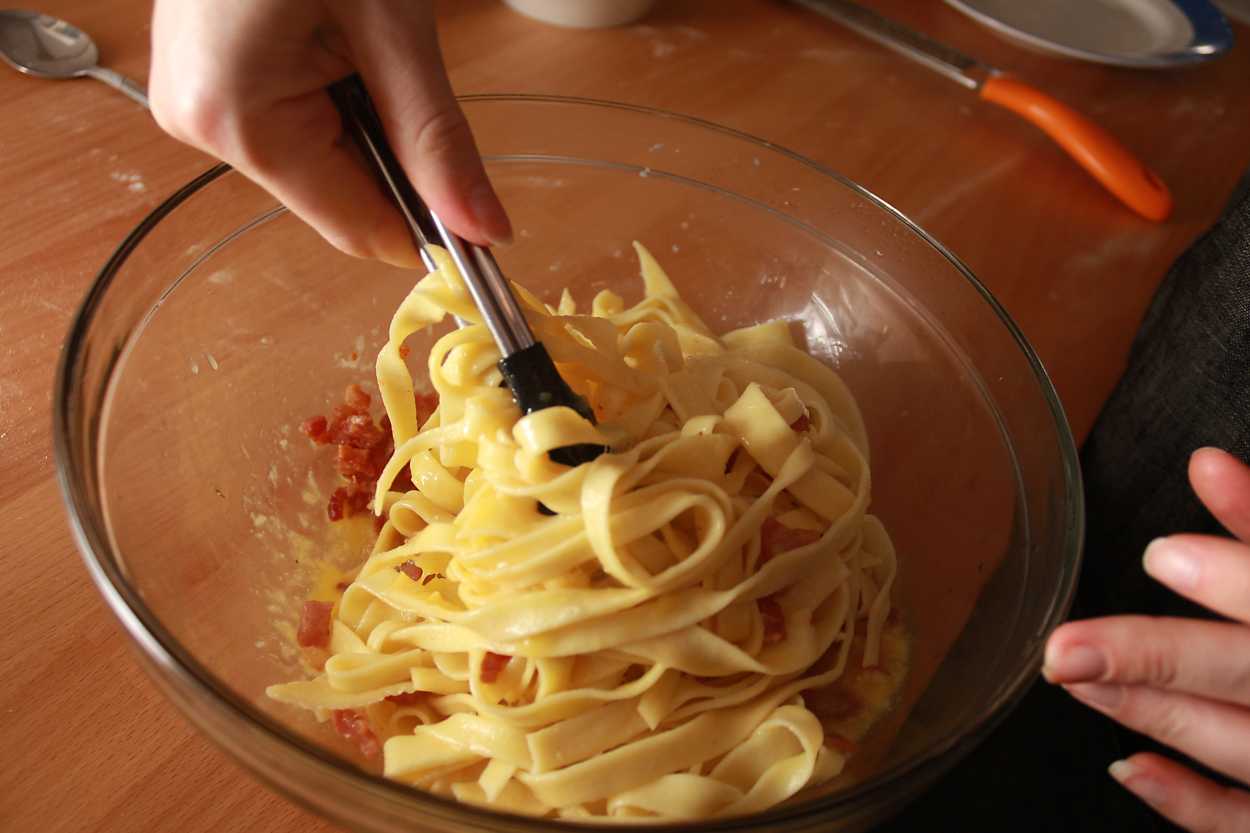 Alyssa tosses noodles in the carbonara sauce