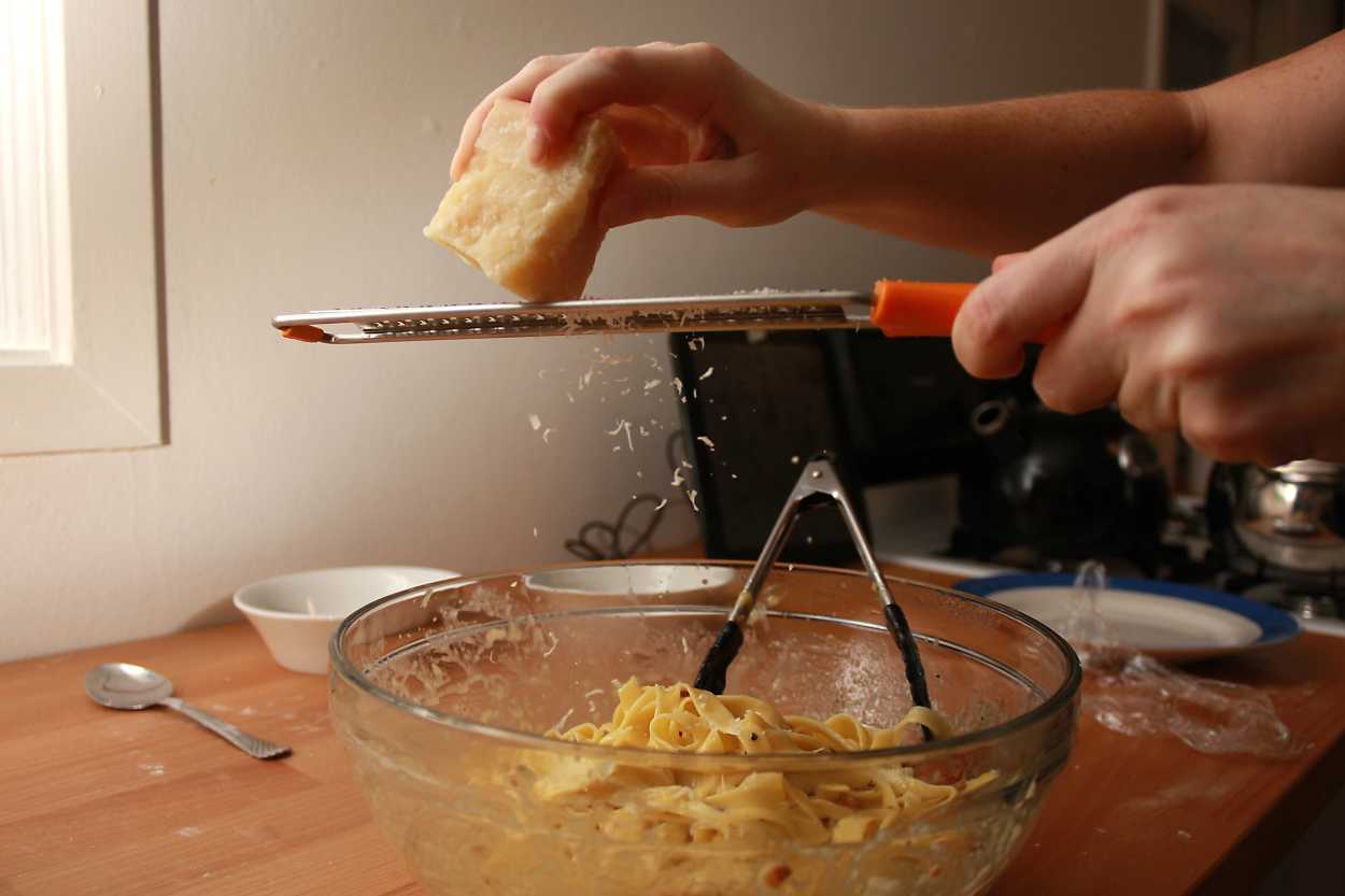 Alyssa grates cheese on top of pasta carbonara