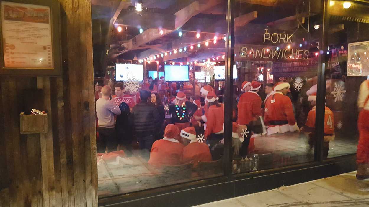 A bar with a bunch of people dressed as Santa inside