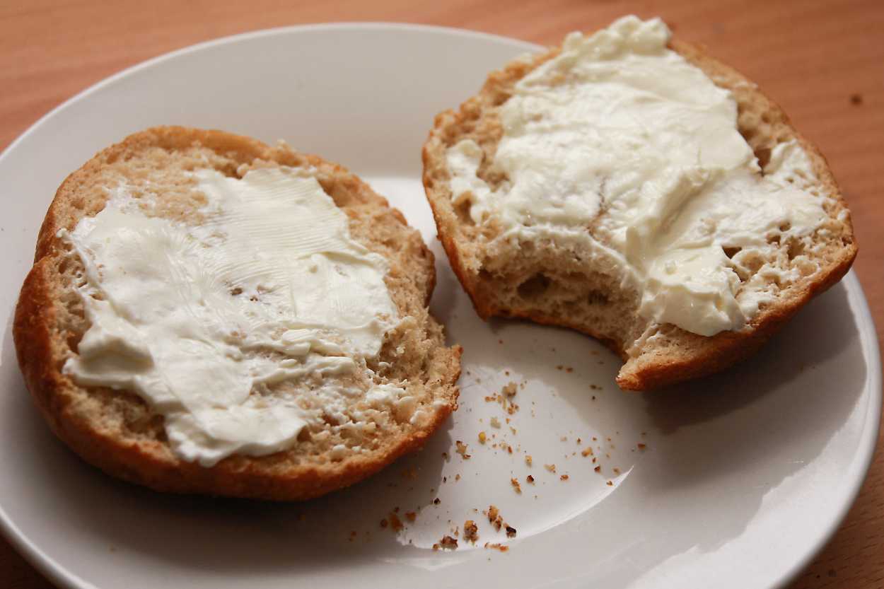 a homemade bagel is split and topped with cream cheese