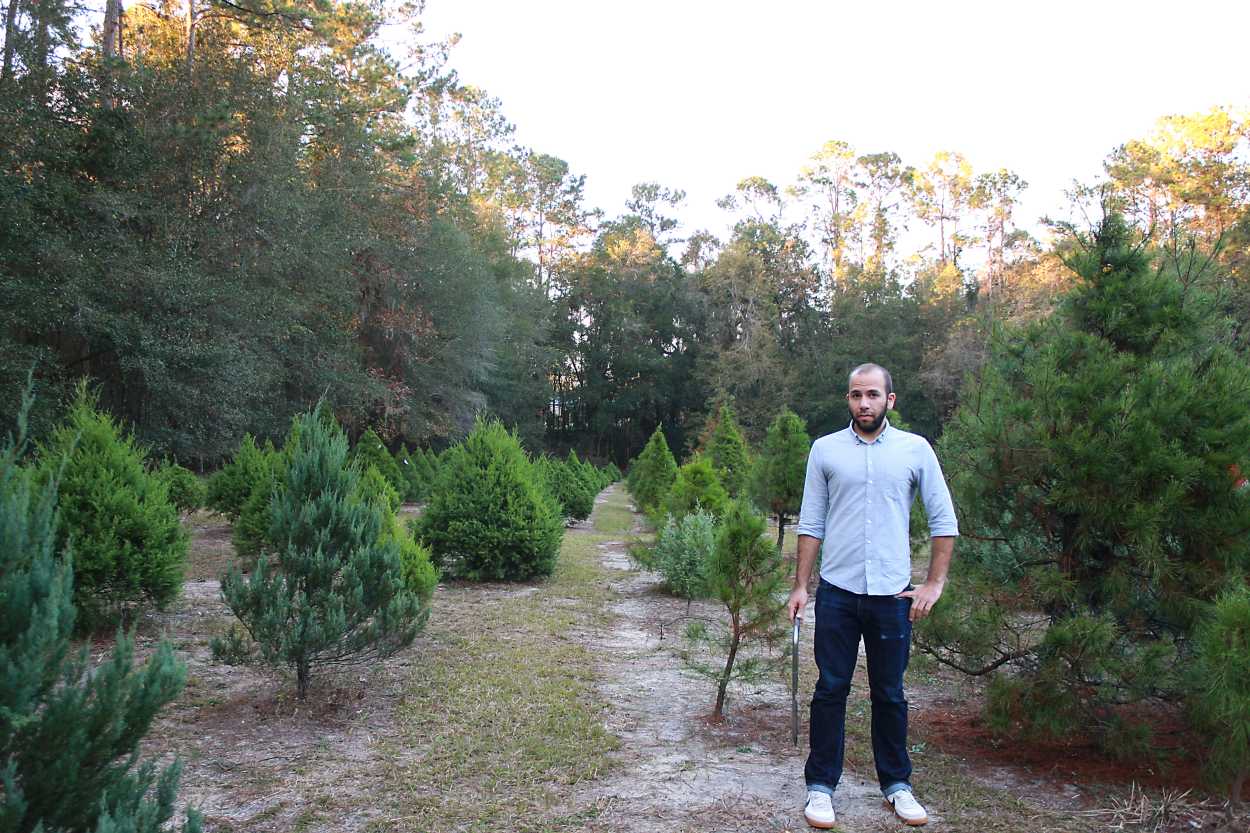 Michael stands at a Christmas Tree Farm with a saw in his hand