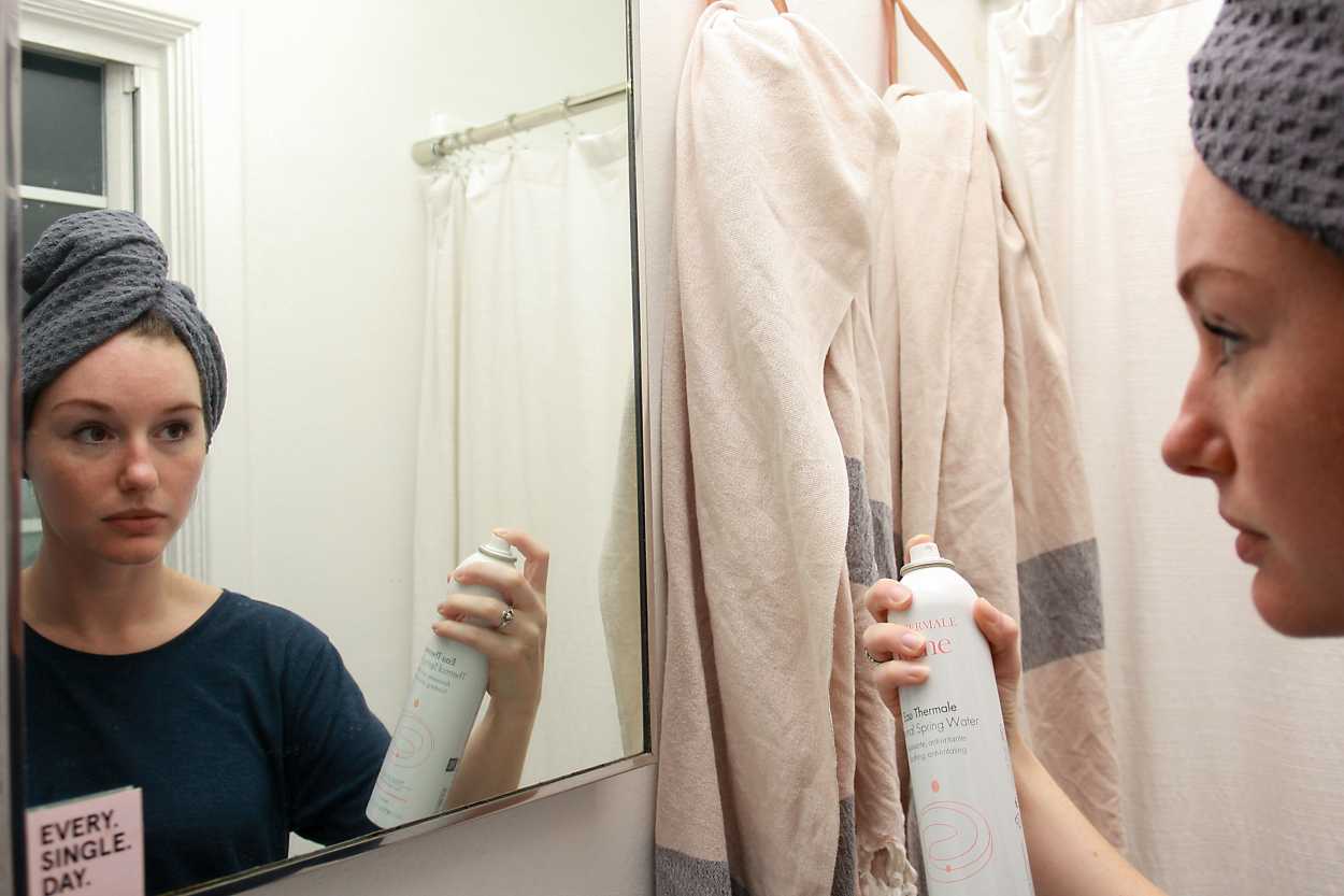 Alyssa sprays Avene thermal water in front of the mirror