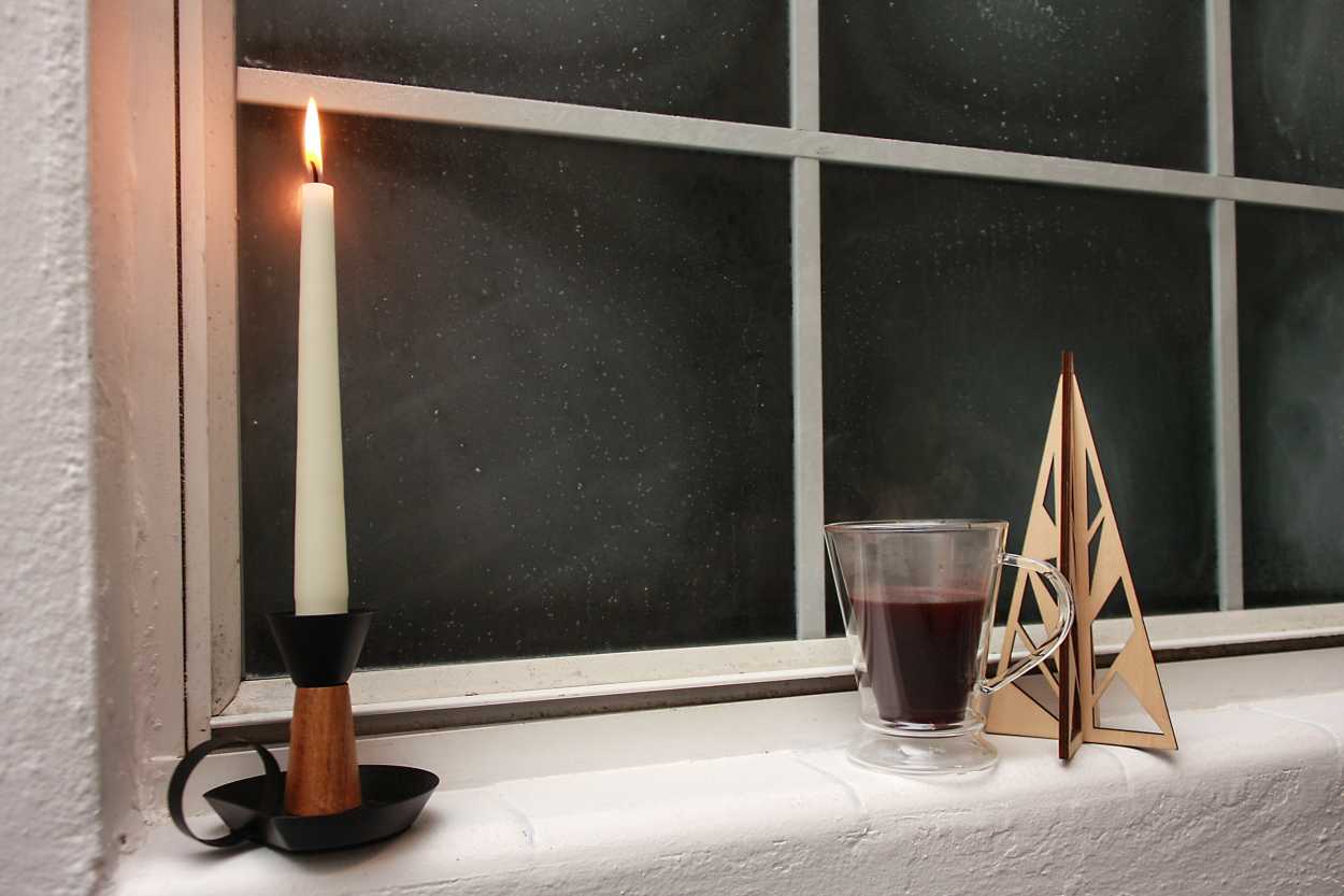 A mug of glogg in a window with a lit candle