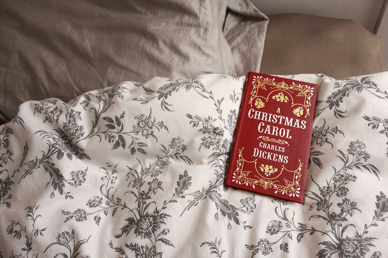 A Christmas Carol book laid by a bed pillow
