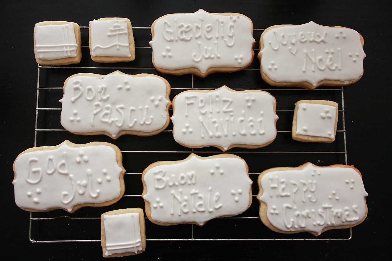 travel inspired christmas cookies that say Merry Christmas in different languages