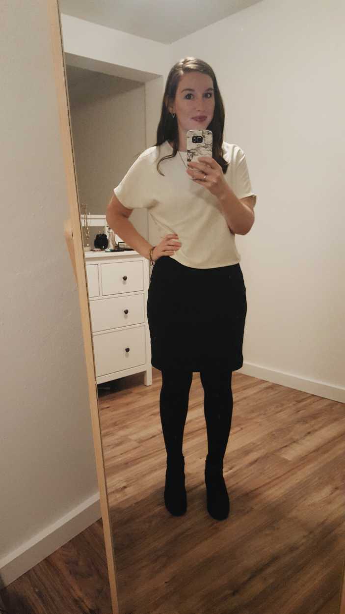 Alyssa wears a white silk tee over a black dress with tights and boots in the evening