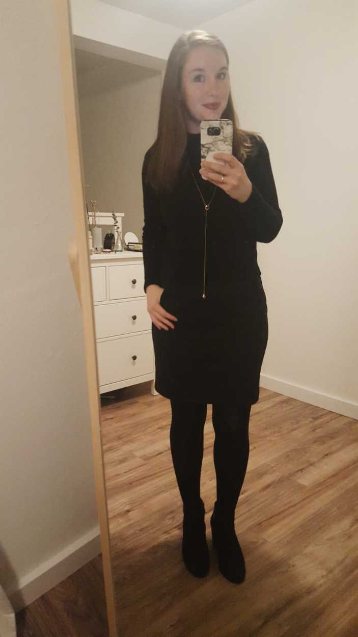 Alyssa wears a black turtleneck sweater over a black dress with tights and boots
