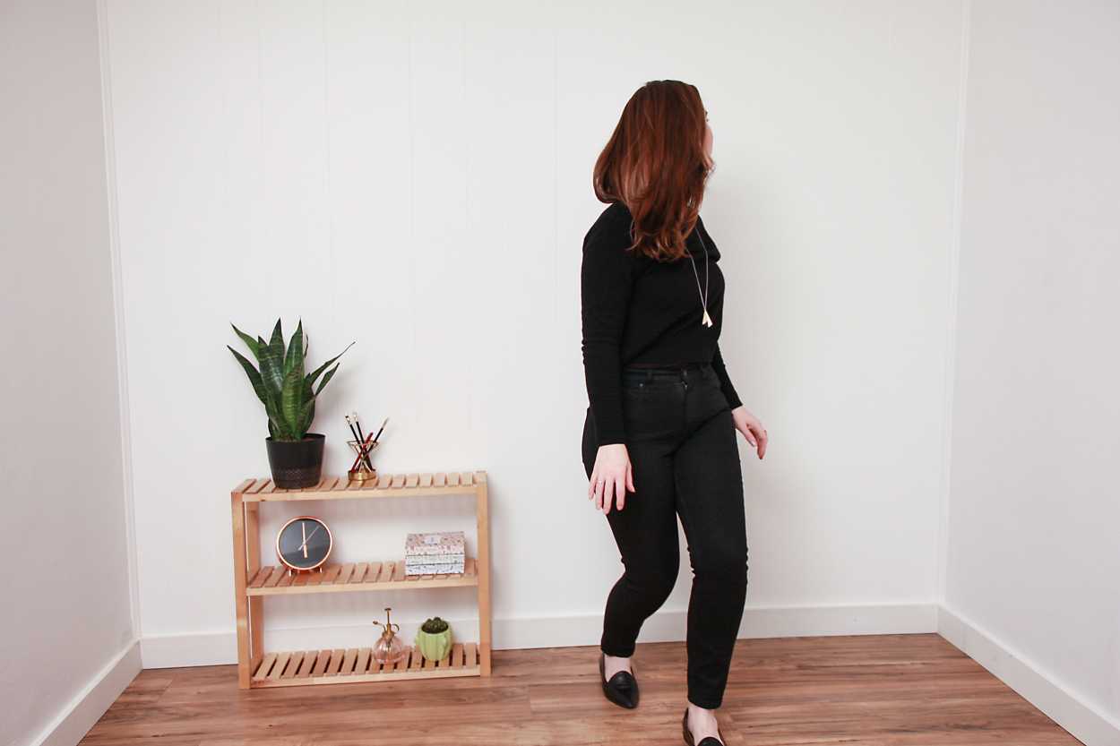 Alyssa wears a black sweater, black jeans, and black flats while looking away from the camera