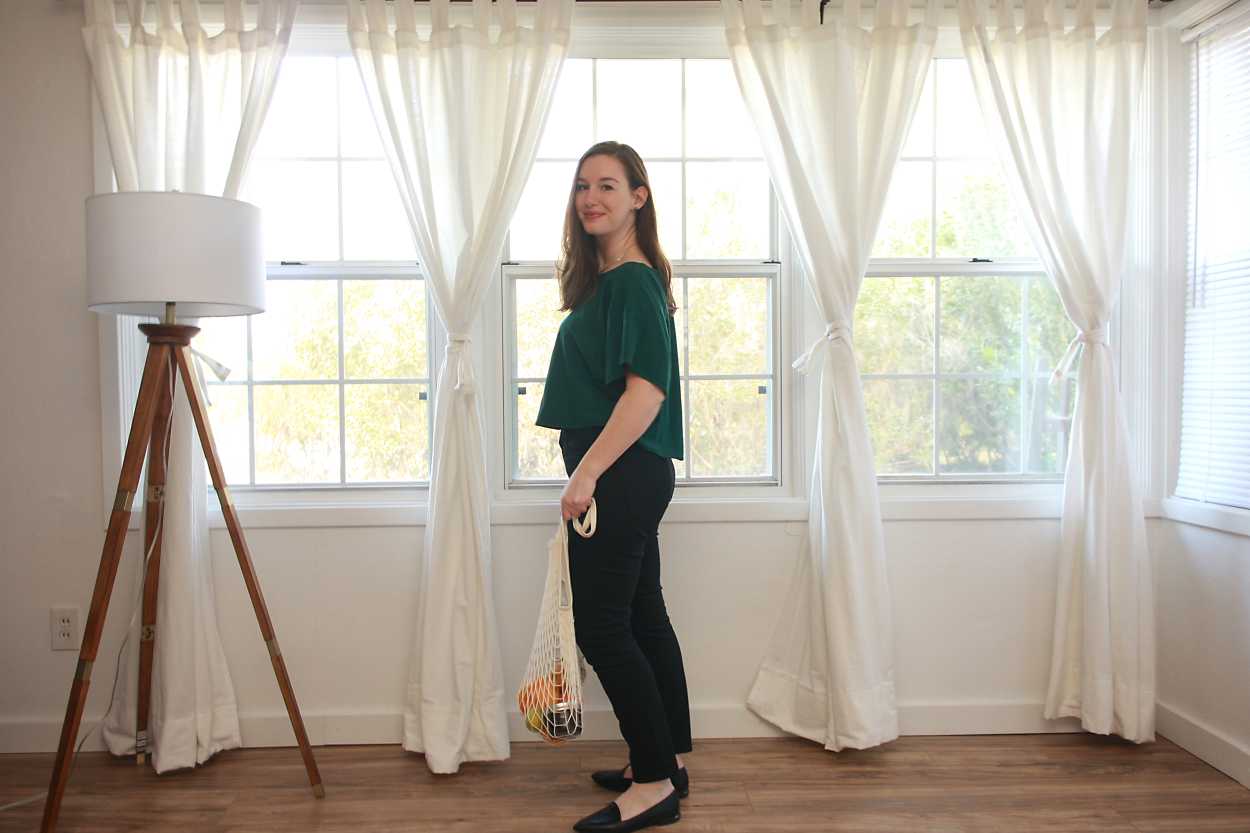 Alyssa wears a green top, black jeans, and black flats while facing sideways