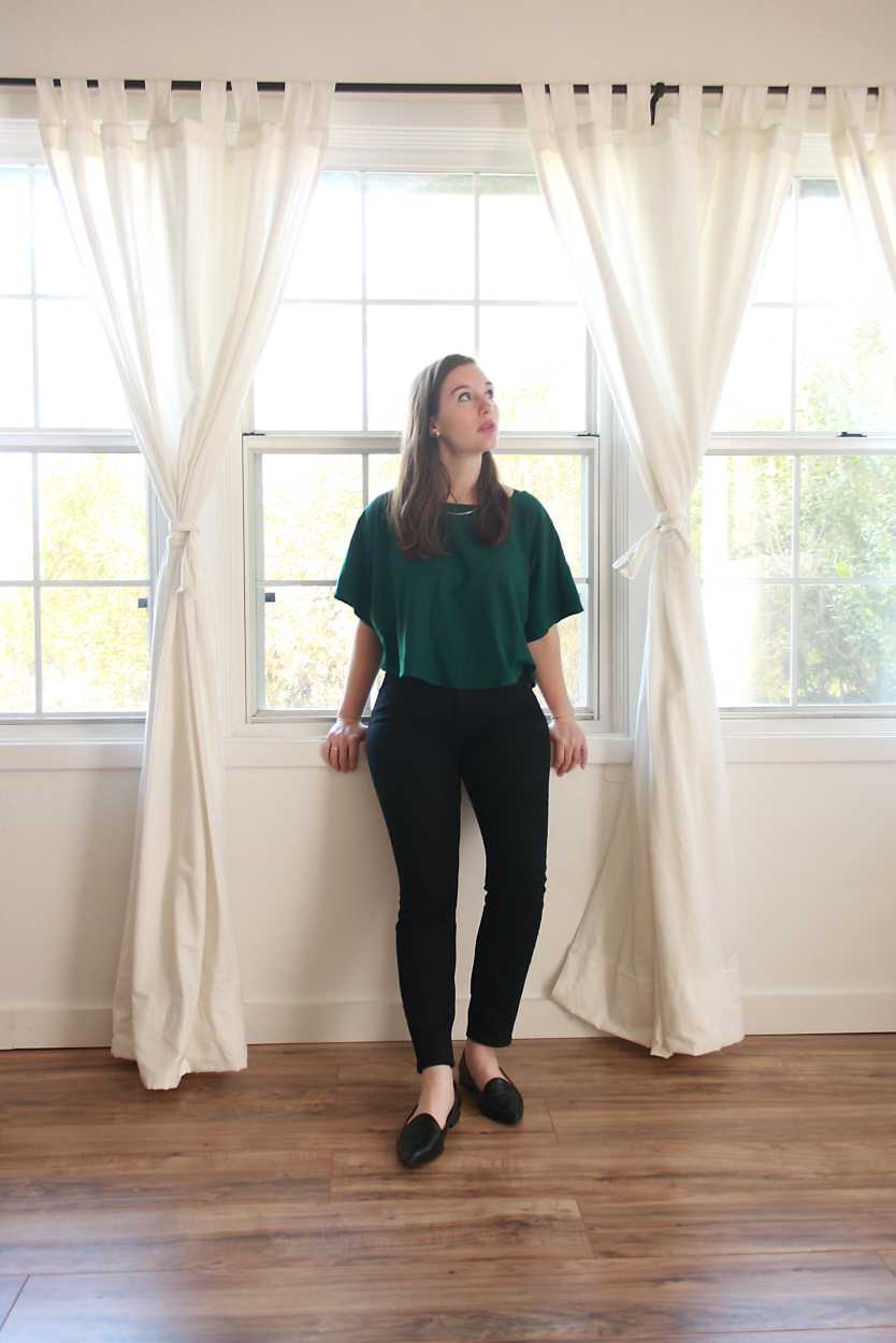 Alyssa wears a green top, black jeans, and black flats while sitting in the window ledge