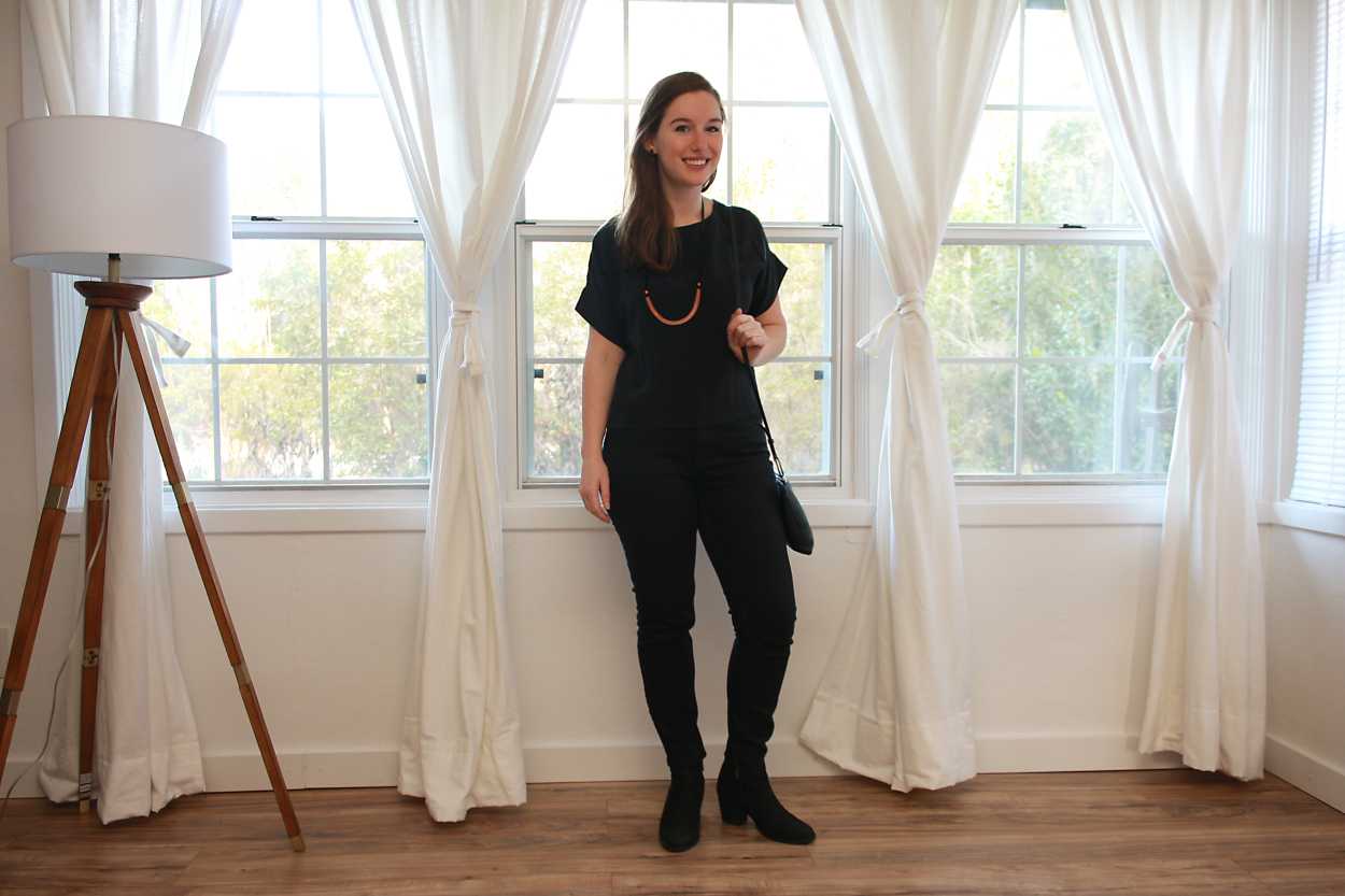 Alyssa wears a black silk tee with black jeans and boots while smiling at the camera