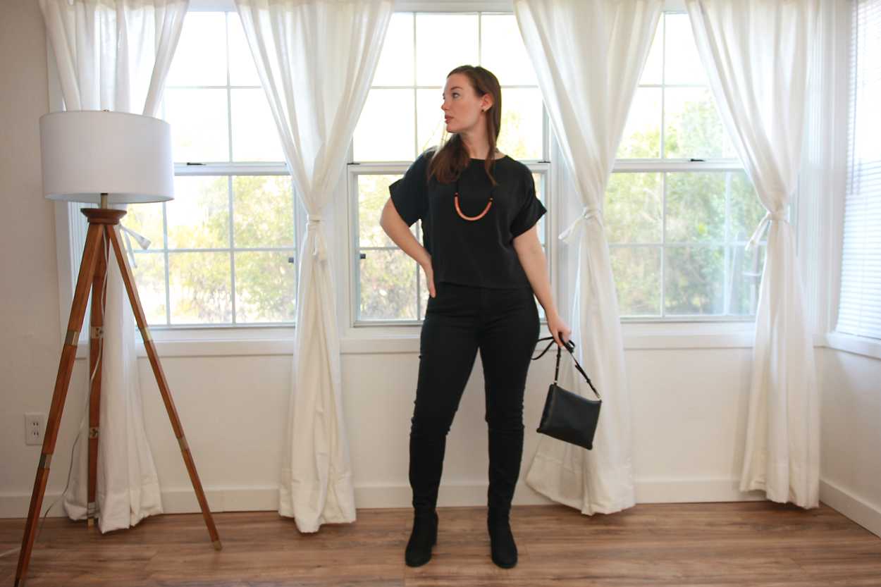 Alyssa wears a black silk tee with black jeans and boots while dangling her purse at her side