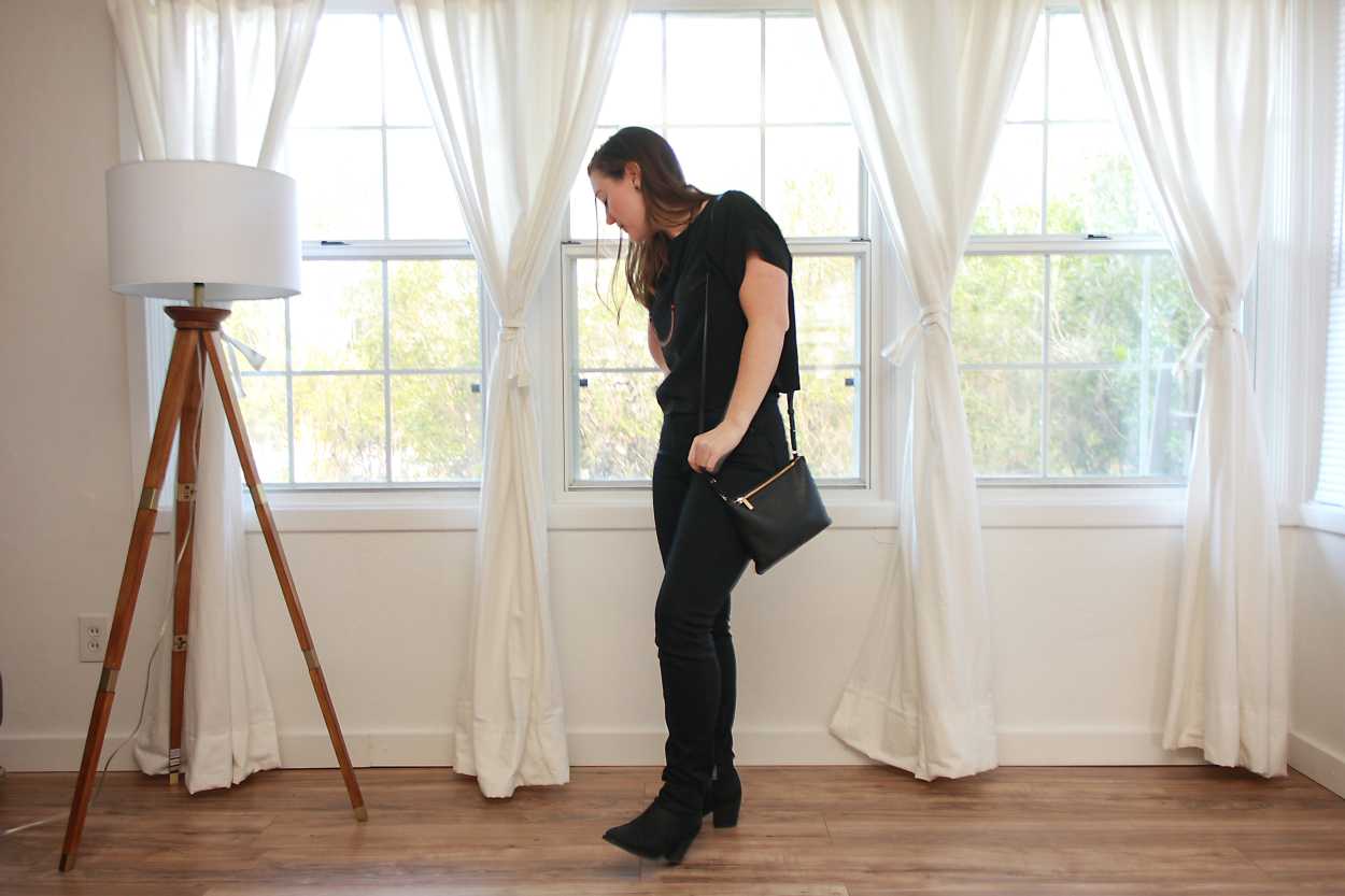 Alyssa wears a black silk tee with black jeans and boots and carries a purse