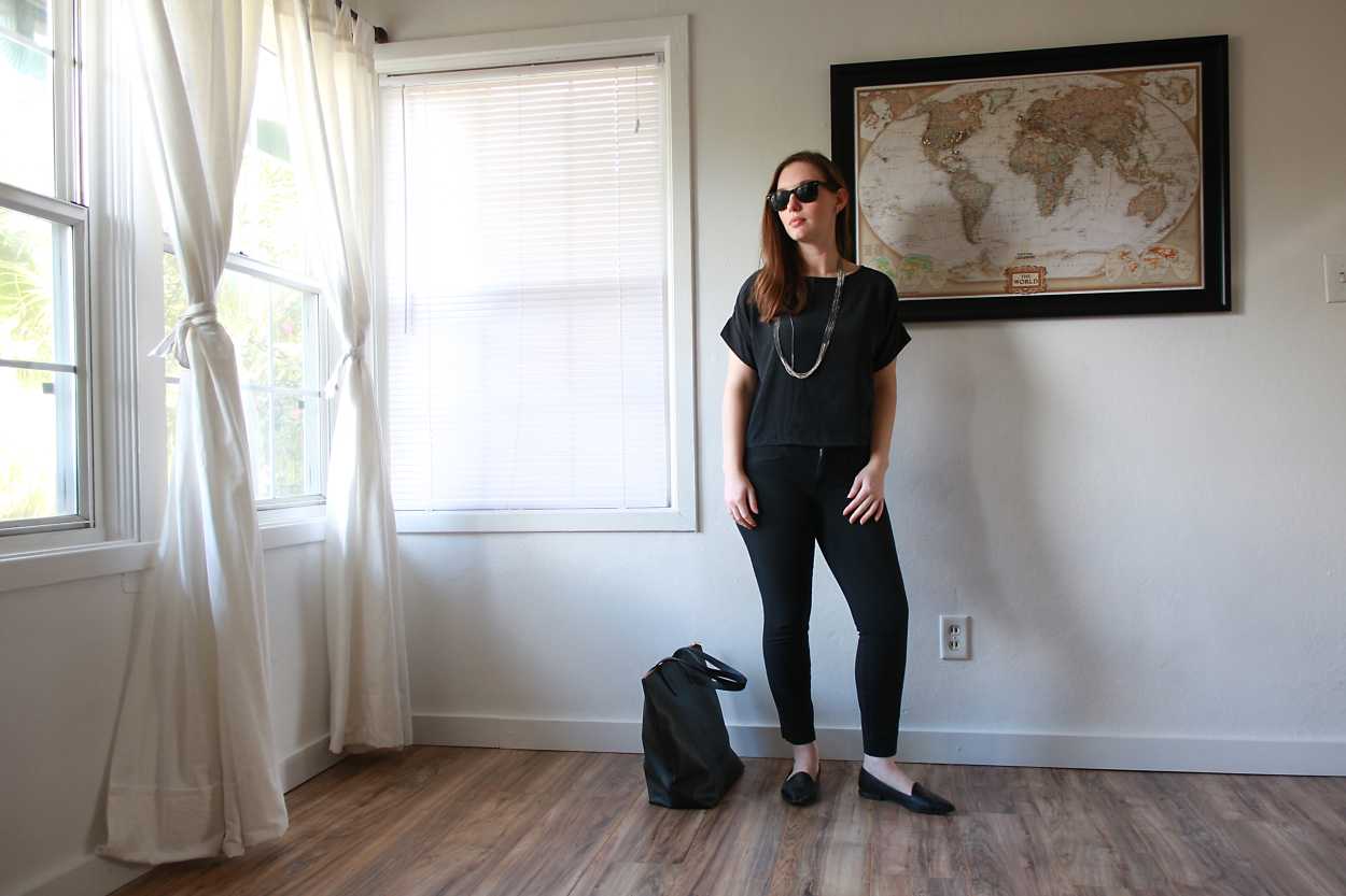 Alyssa wears a silk tee, black pants, and black flats with sunglasses and a tote