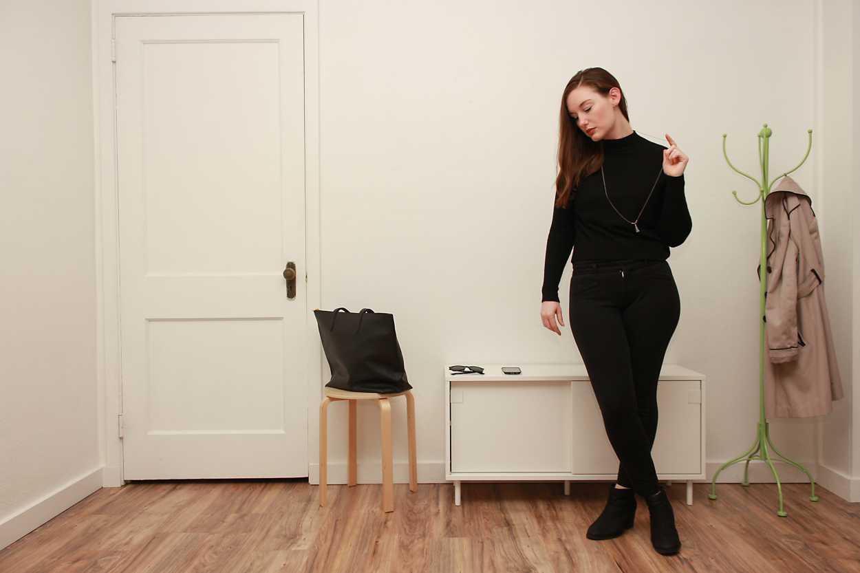 Alyssa wears a black cashmere mockneck sweater with black pants and boots and fiddles with her necklace