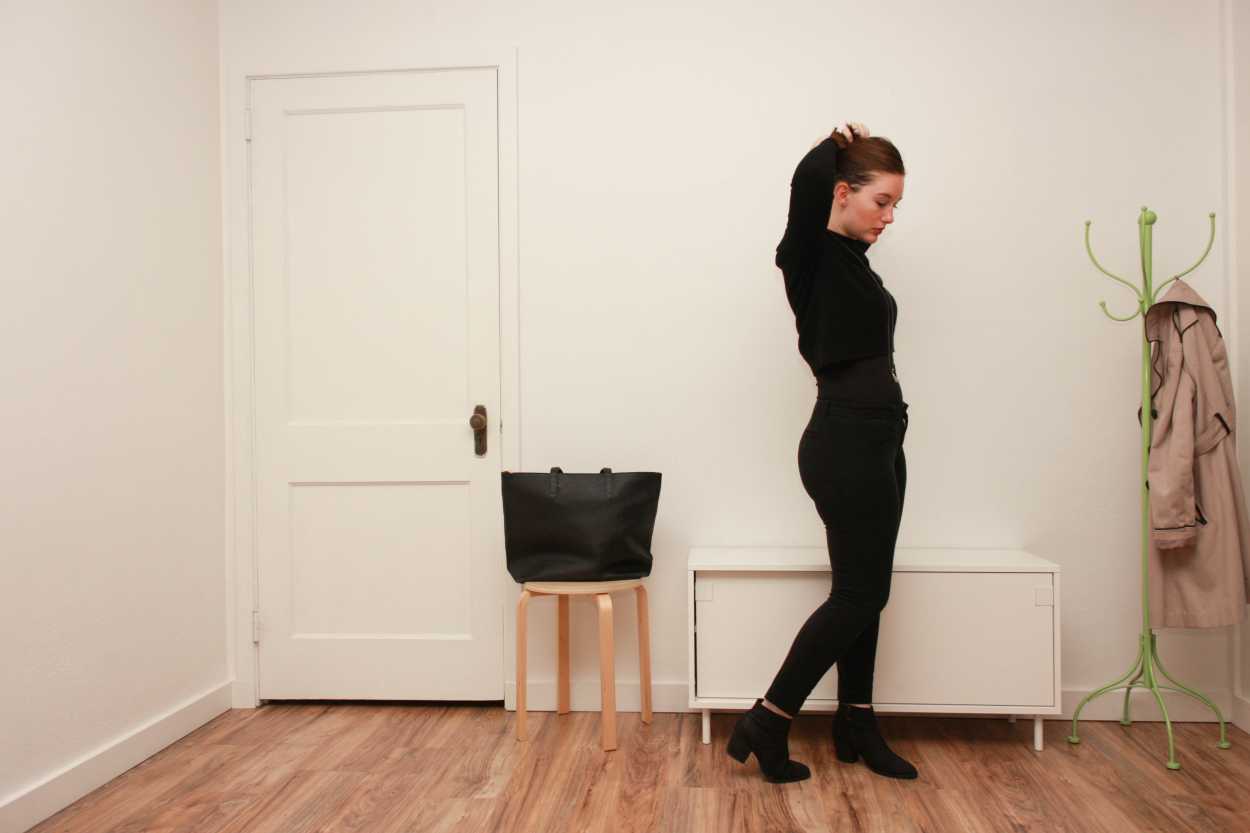 Alyssa wears a black cashmere mockneck sweater with black pants and boots and looks downward
