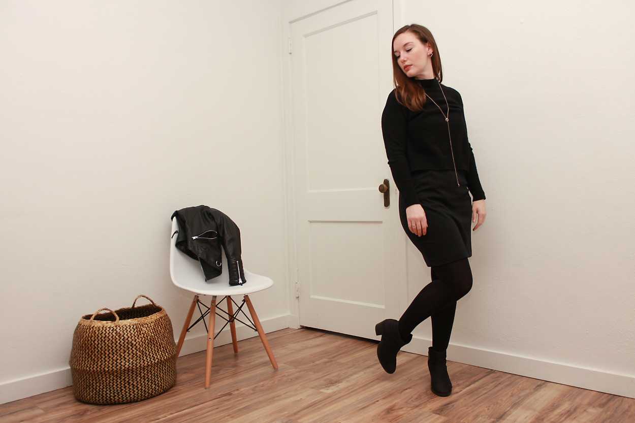 Alyssa wears a black turtleneck sweater over a black dress with tights and boots and looks away