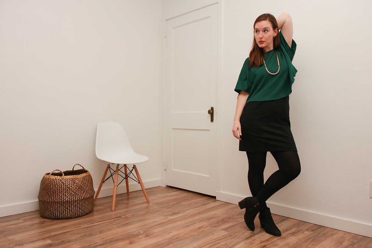 Alyssa wears a green silk top over a black dress with tights and boots