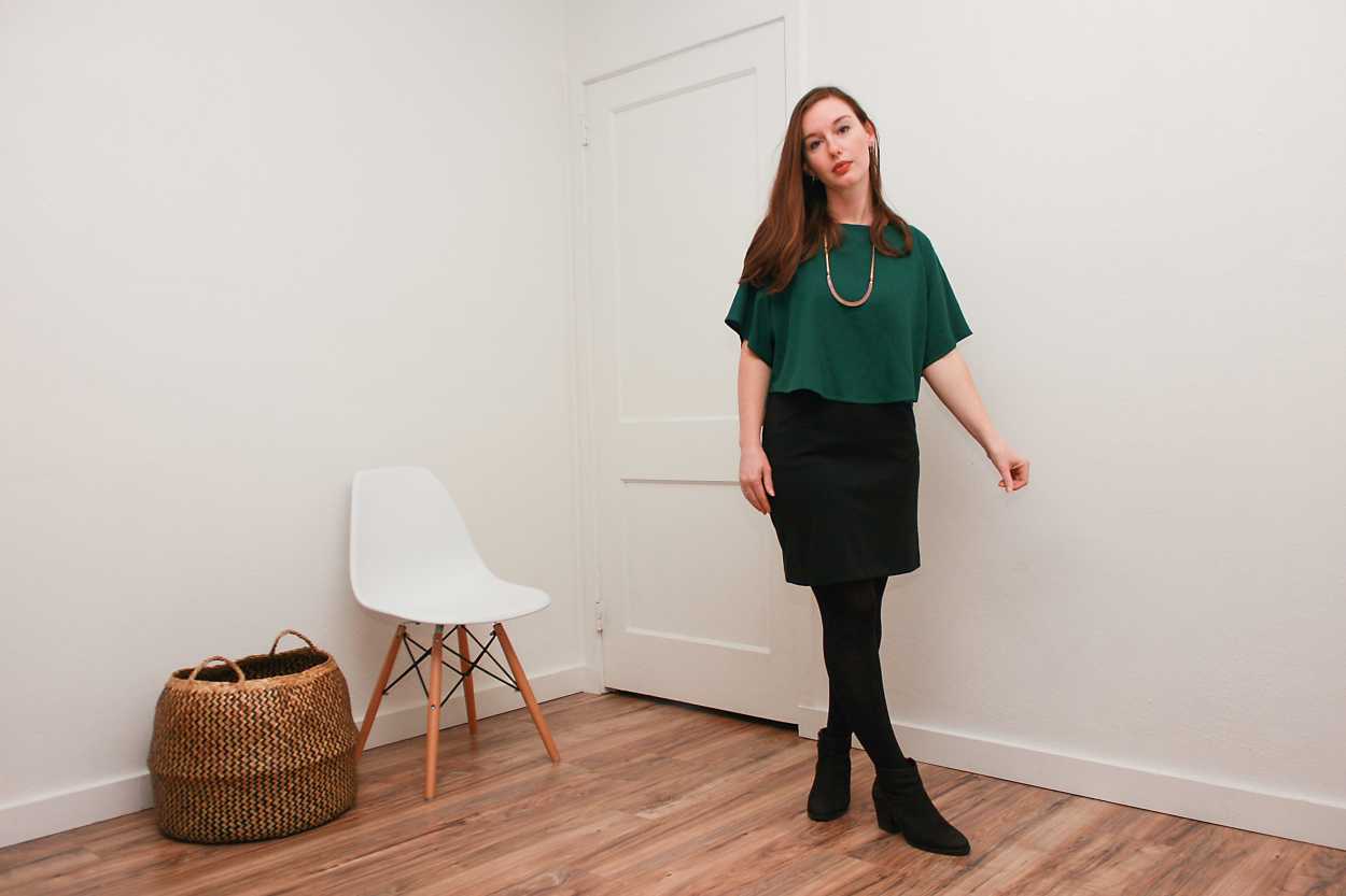 Alyssa wears a green silk top over a black dress with tights and boots