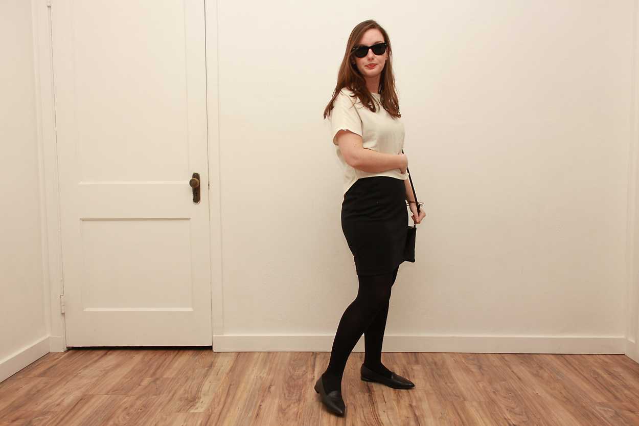 Alyssa wears a white silk tee over a black dress with tights and flats while holding a black purse