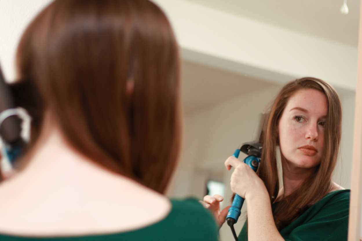 a woman using a curling iron in the mirror