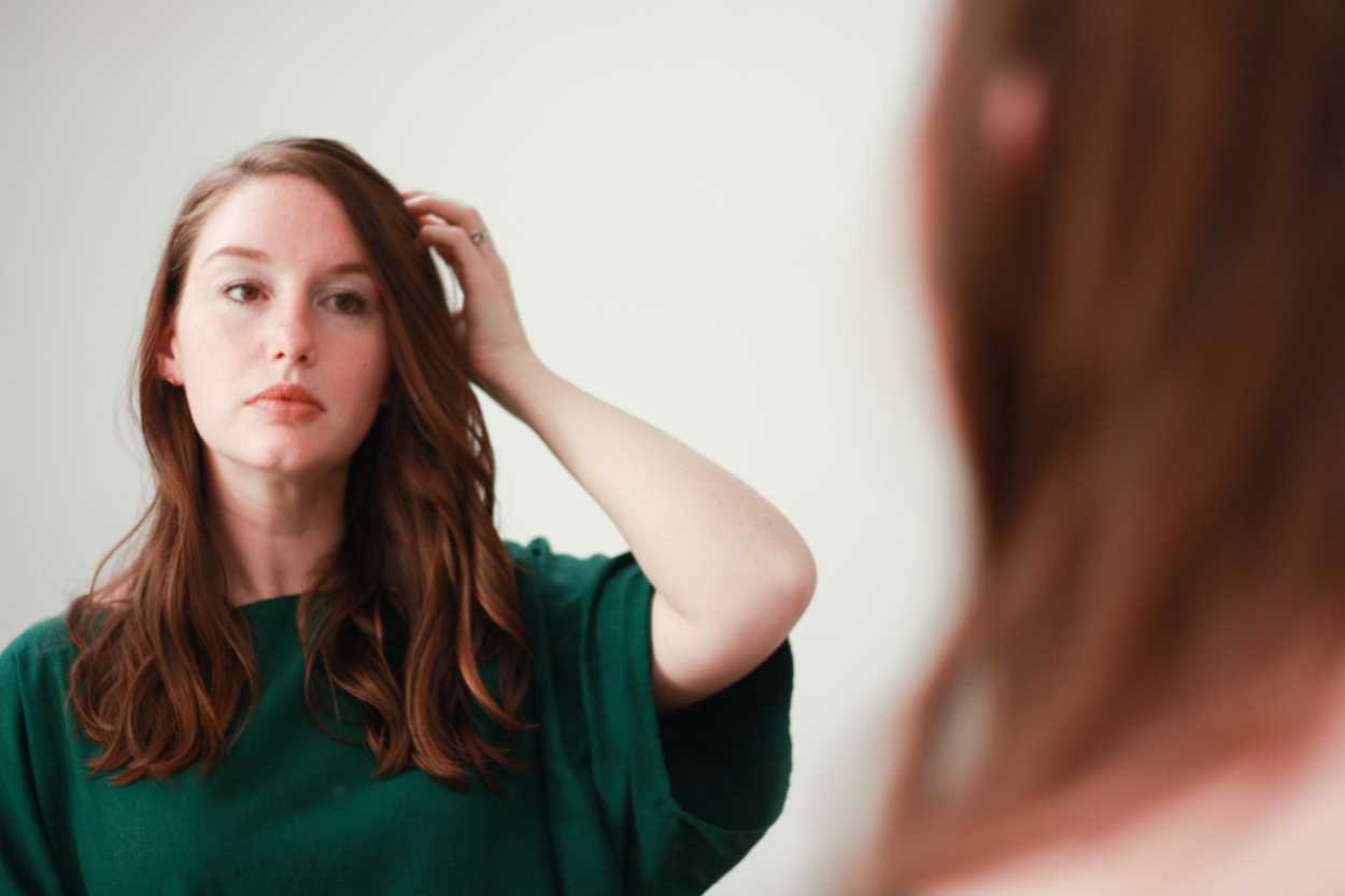 a woman with loose waves looks in the mirror and adjusts her hair