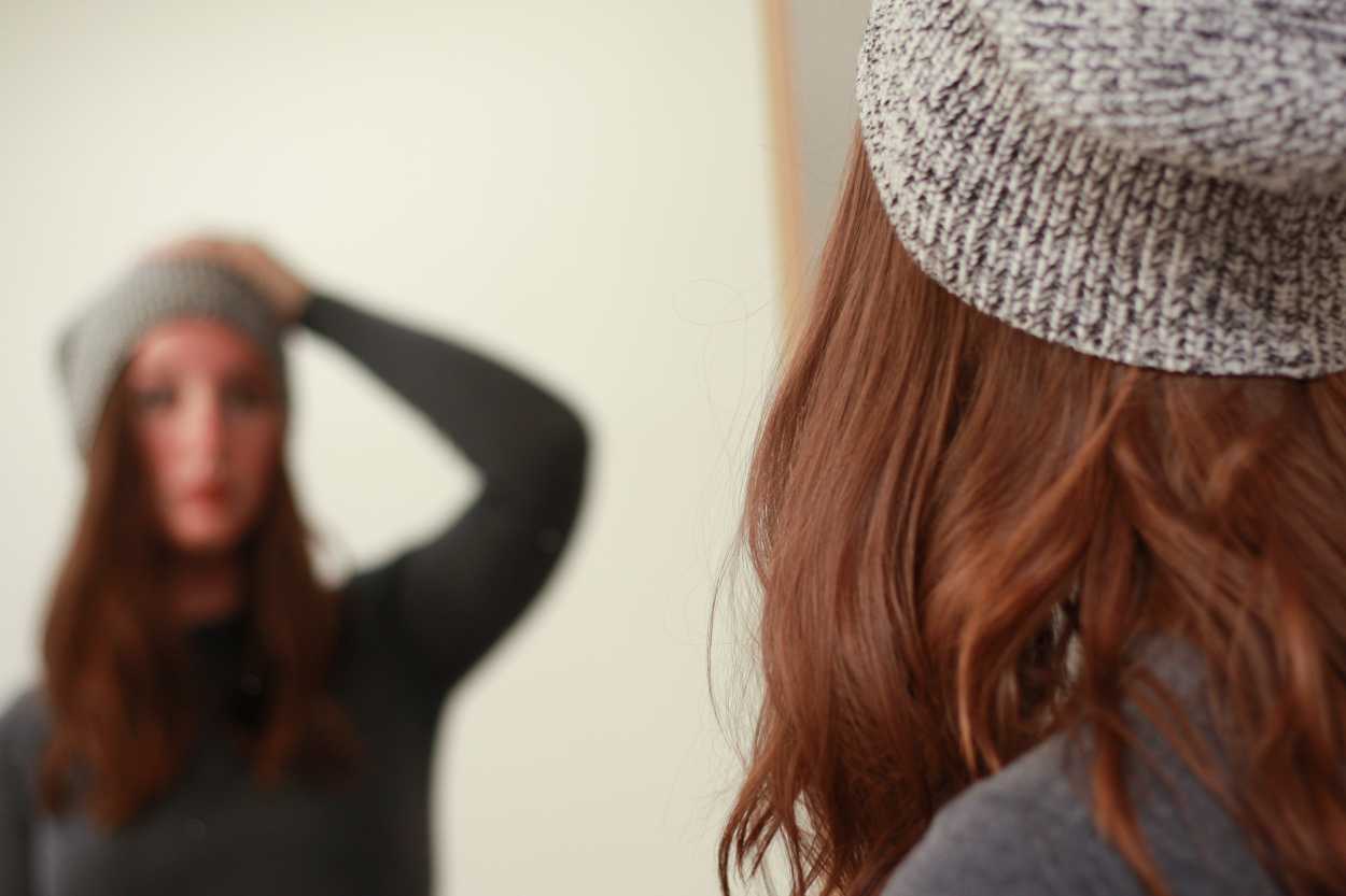 a woman adjusting her beanie in the mirror