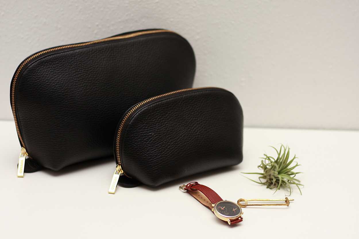 The Leather Travel Case Set from Cuyana sits on a counter next to a watch, pin, and airplant