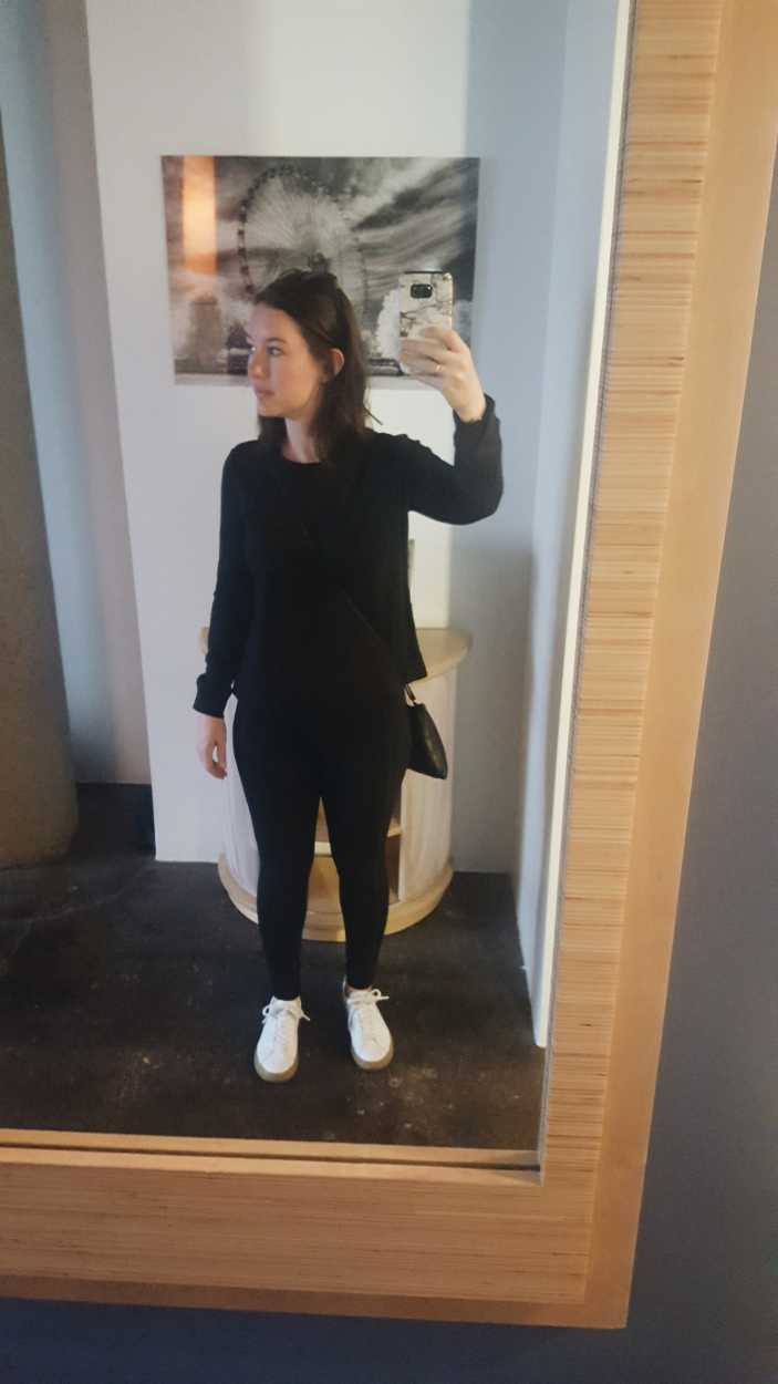 Alyssa wears an all-black outfit and takes a photo in the mirror