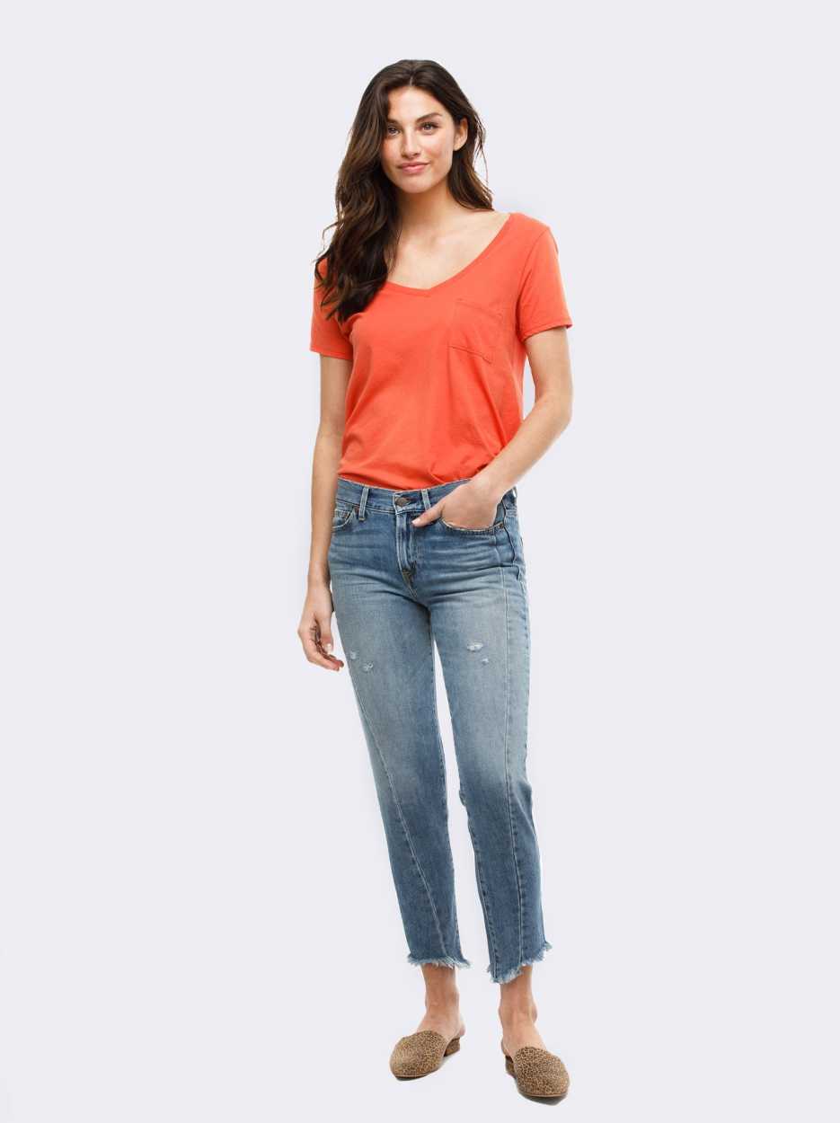 A woman wears a red-orange shirt and blue jeans