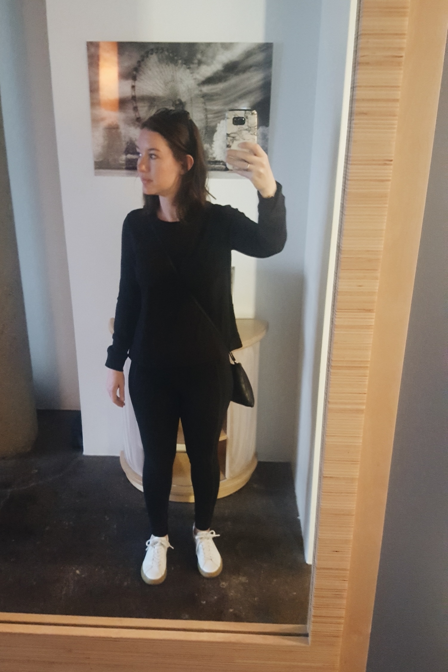 Alyssa wears an all-black outfit and takes a photo in the mirror