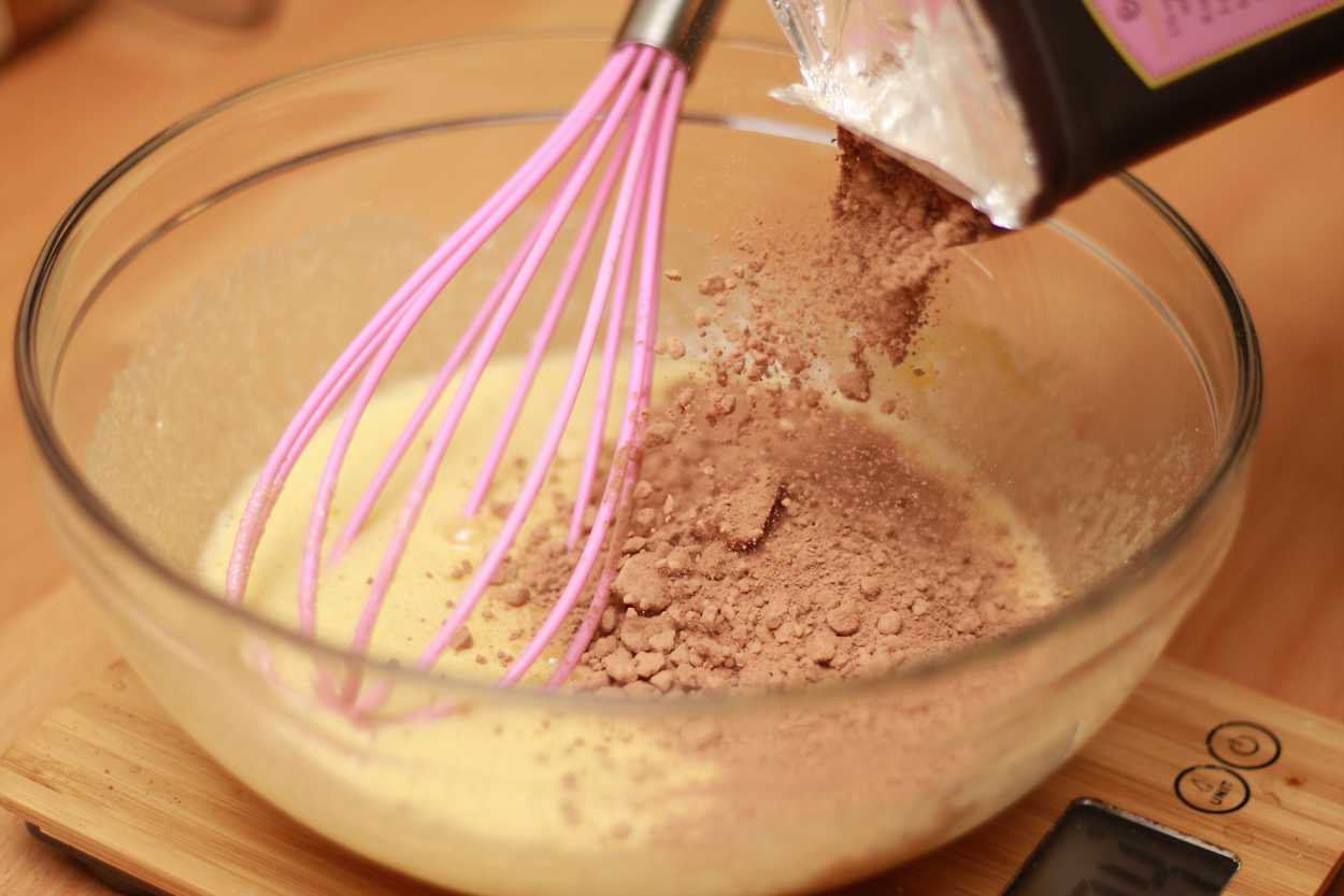 cocoa powder is shaken into a bowl of beaten eggs and sugar